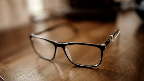 A pair of black eyeglasses resting on a wooden desk in a warm interior