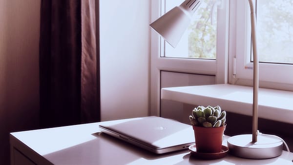 A laptop and a lit lamp on a wooden table in a darkened room