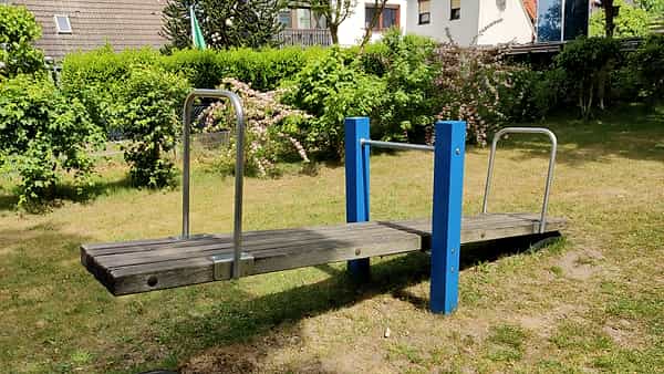 A playground seesaw standing empty, its pivot in the center of the frame
