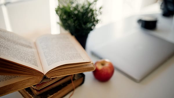 An open book and a laptop on a table with an apple beside them