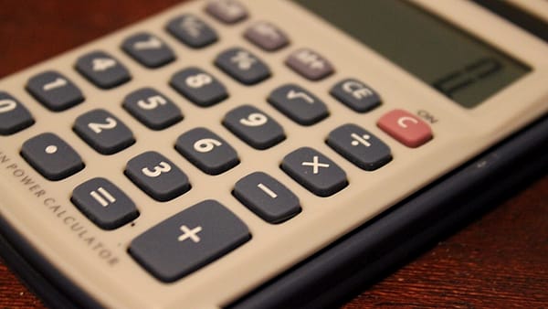 A basic desk calculator photographed on a plain surface beside a notepad