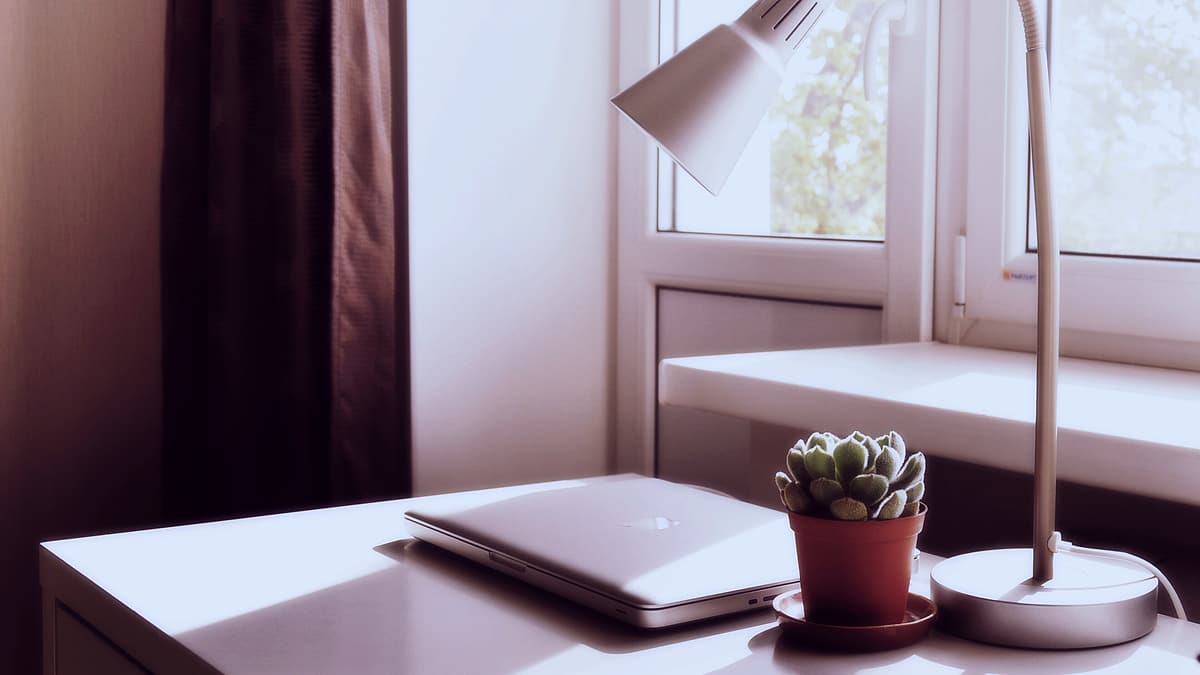 A laptop and a lit lamp on a wooden table in a darkened room