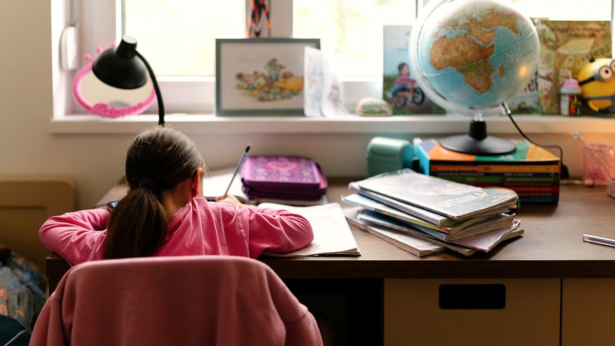 A child working at a desk by a window with a globe and books beside them