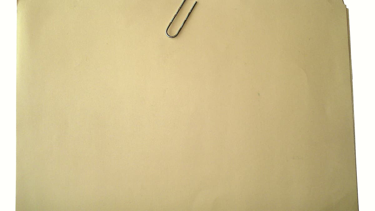 A manila folder lying closed on a desk with a paperclip resting on top of it
