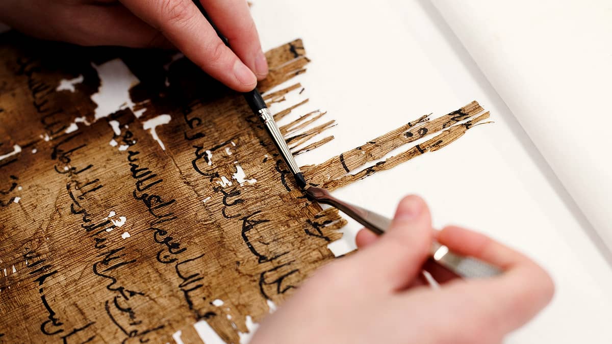 A paper conservator working on fragments of an ancient document at a bench